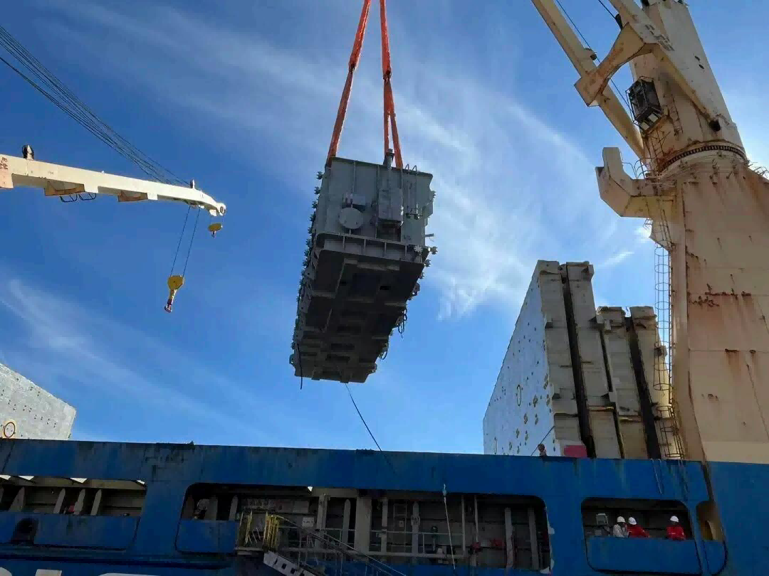 128-ton transformer suspended above the vessel deck with orange lifting slings and red quay crane in frame